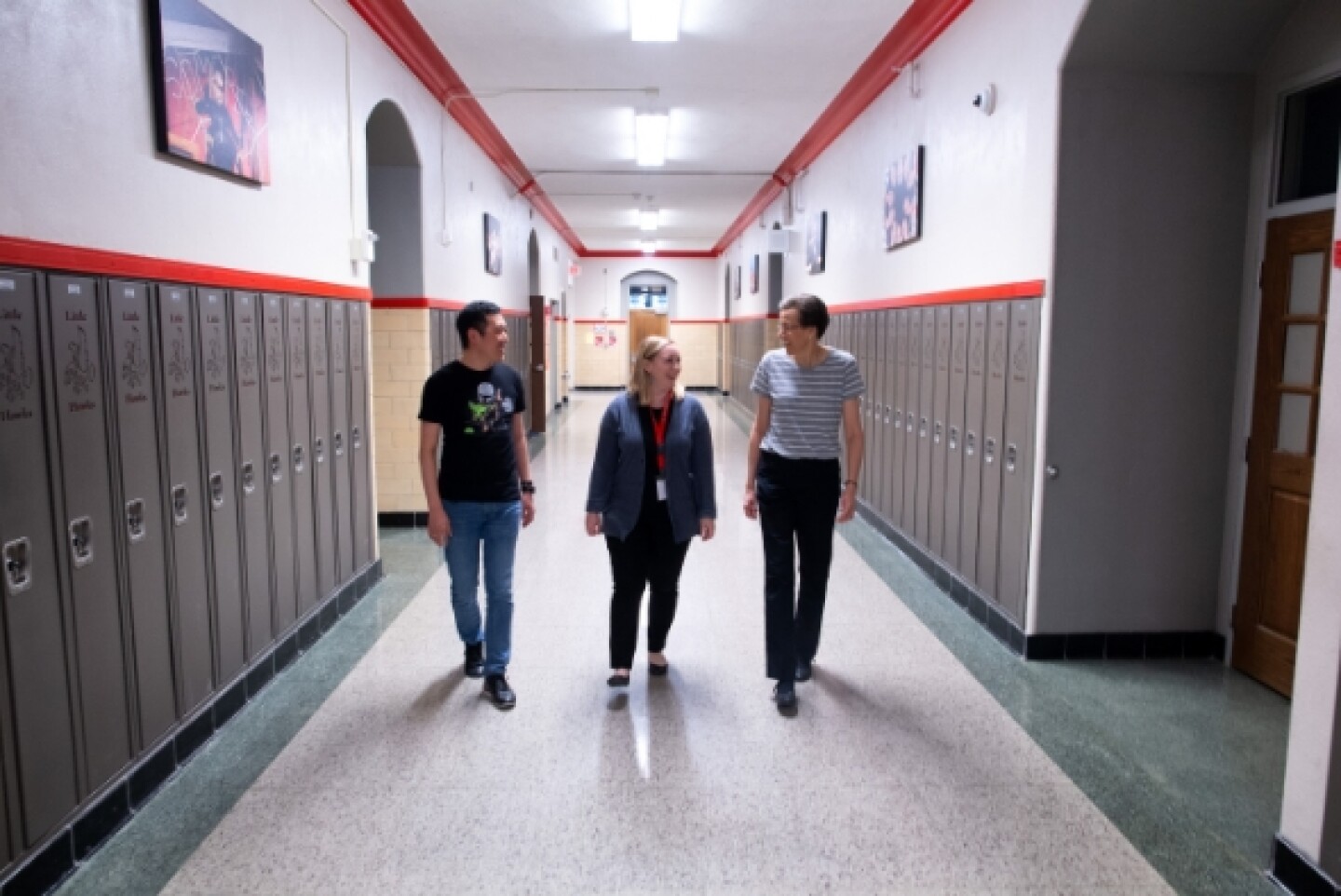 Three educators walking through a school hallway with lockers
