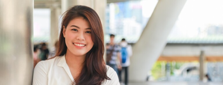Smiling woman stands on a bridge underneath a highrise building
