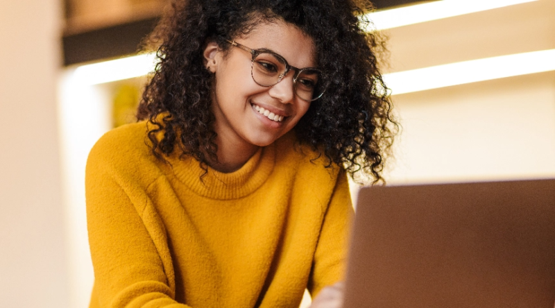 Woman smiling while focused on her laptop, actively completing work tasks.