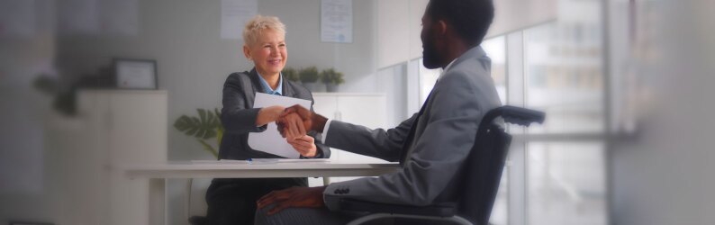 Male disabled job candidate and mature female employer shaking hands and smiling at camera.