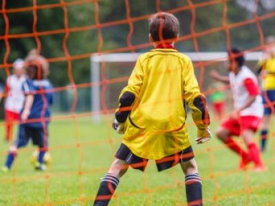 kids-playing-soccer-camera-behind-goalie-in-yellow-orange-net