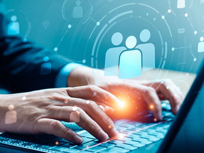 Image of a man in a suit sitting at a laptop. Holographic icons hover over the keyboard.
