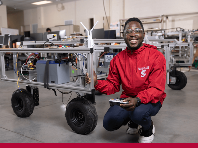 Smiling man in red Santa Clara University shirt next to wheeled engineering project