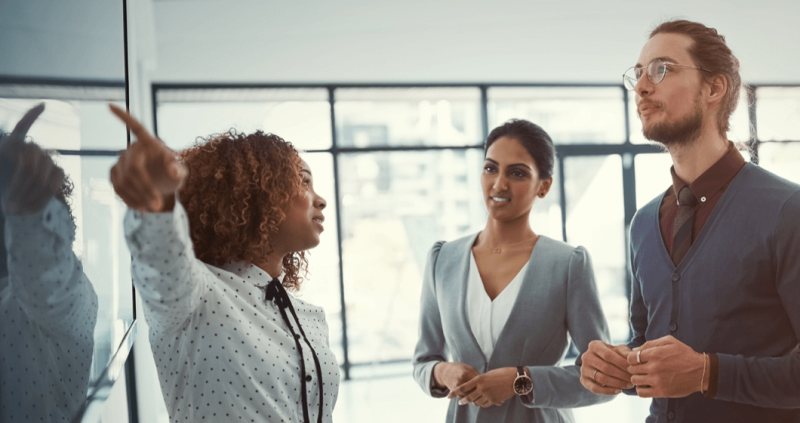 Woman pointing to whiteboard as man and woman look on