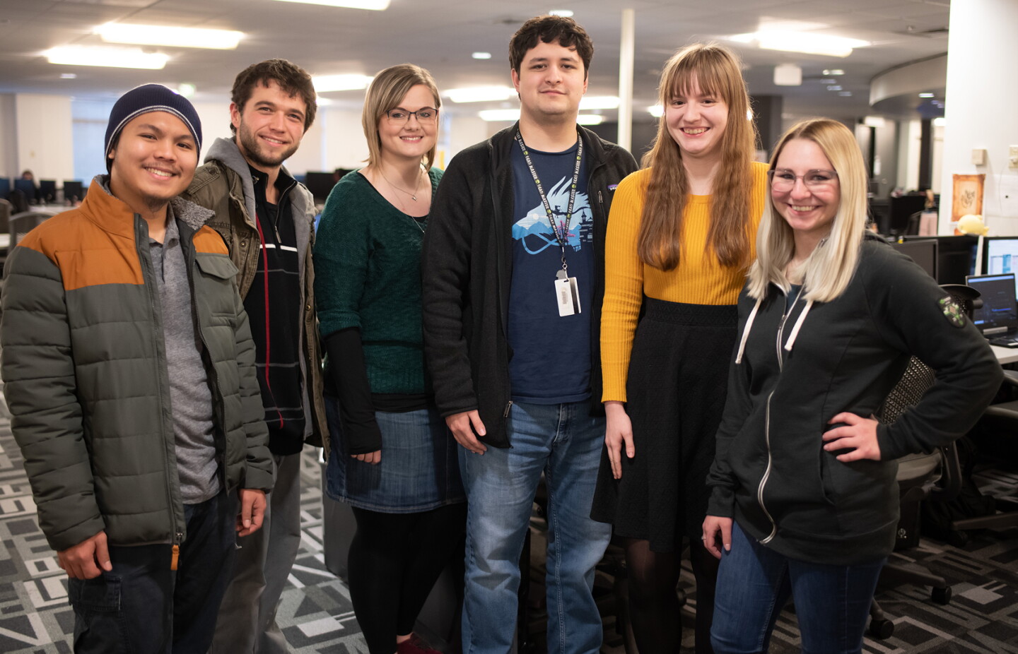 Group of students standing together and smiling in a computer lab or collaborative workspace.