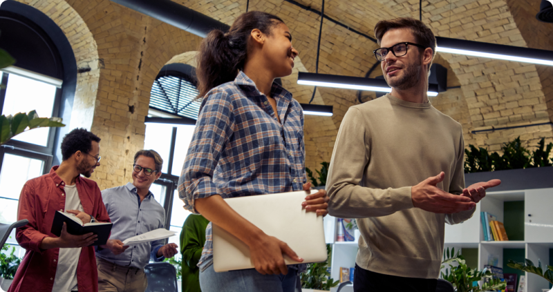 Group of diverse coworkers walking and engaging in a lively discussion in a modern office environment.
