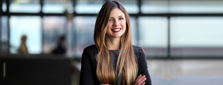 Woman in black long sleeve dress stands smiling in an office space