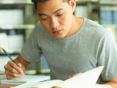 Male student studying and reading book in library