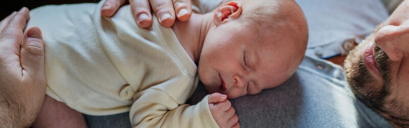 An infant sleeps peacefully on the chest of a bearded man.