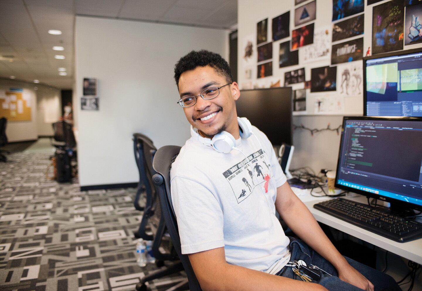 Student seated at a computer in a digital lab, smiling while coding on a desktop computer.