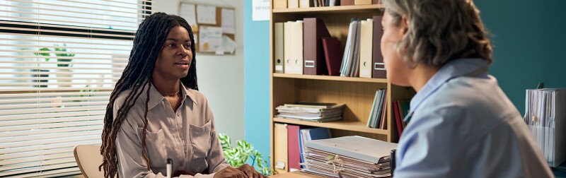 Young Black woman sitting across desk from a social worker