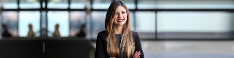 Woman in black long sleeve dress stands smiling in an office space