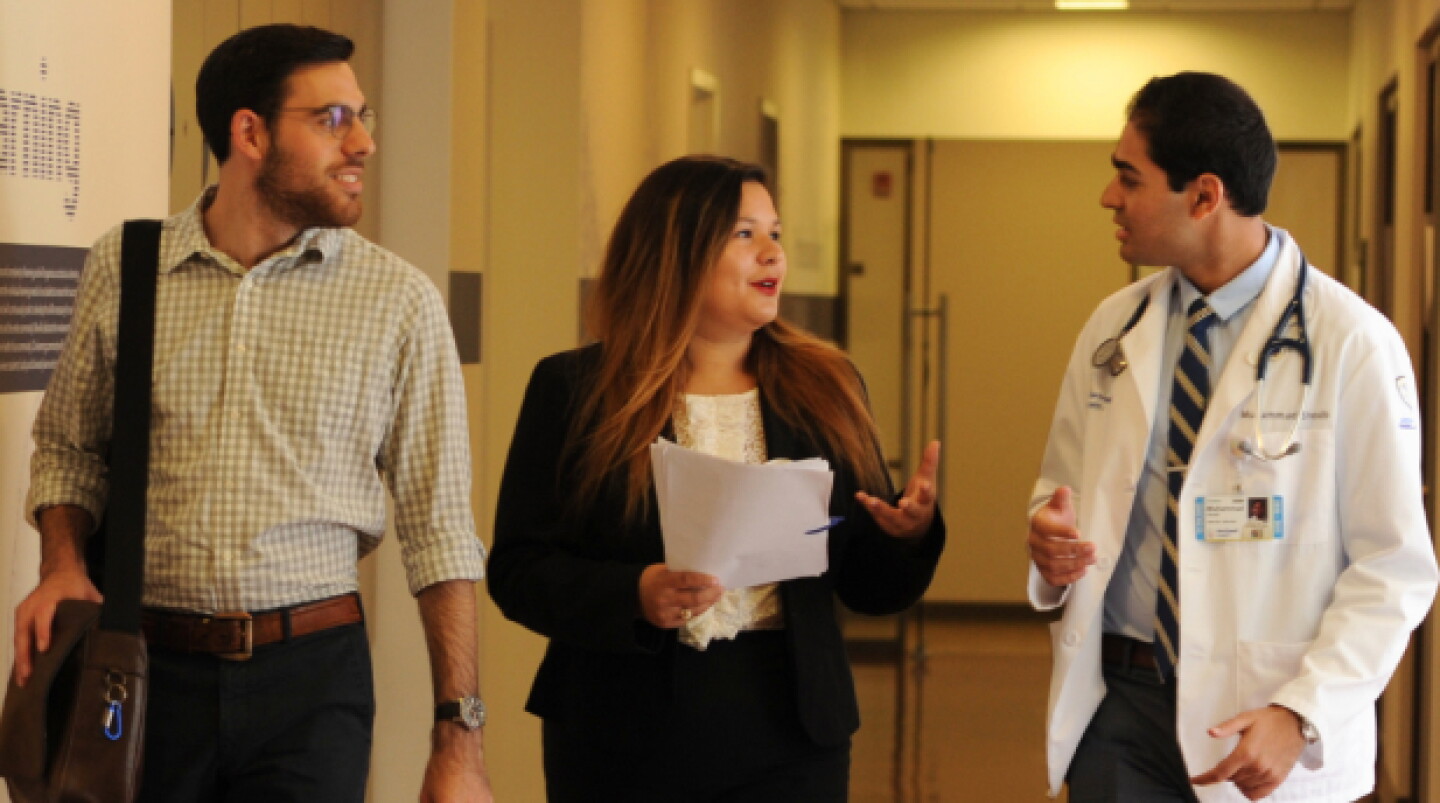 A male and female legal professional converse with male physician in hallway.