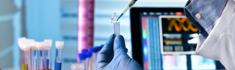 Gloved hands in a lab transfer liquid from a dropper to a vial.