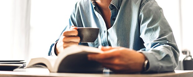 Man drinking coffee and reading one of the best sports management books for your career