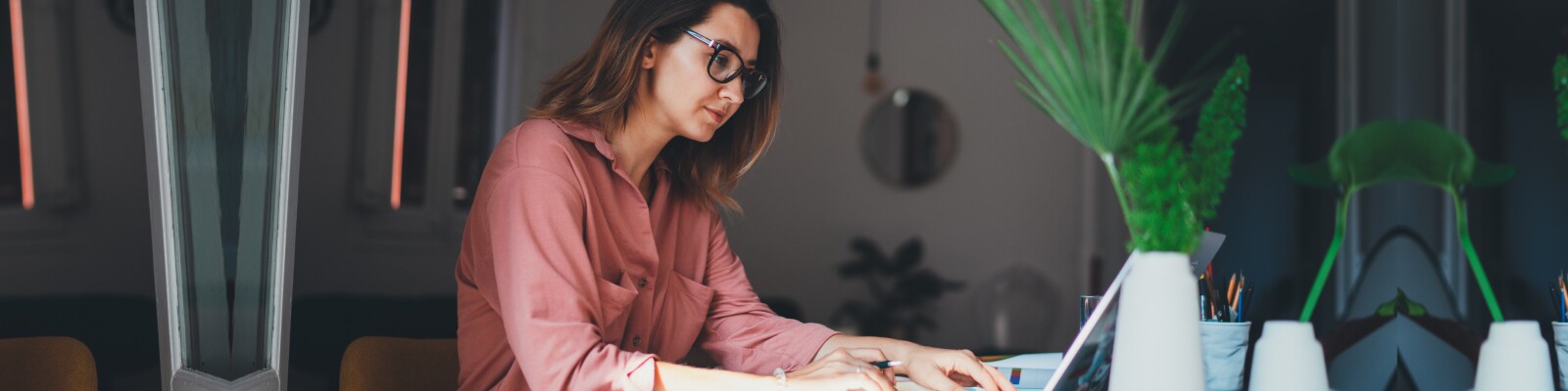 Woman in pink blouse works on her laptop in her home