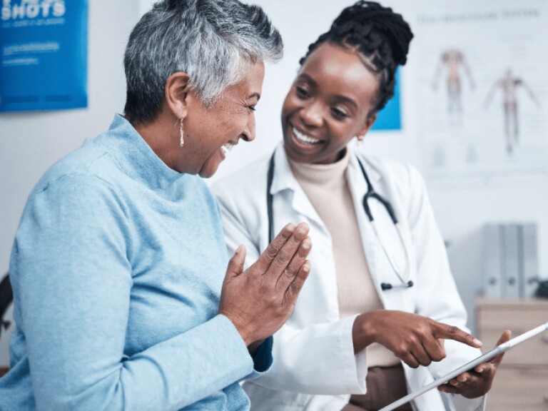 Female doctor with stethoscope showing tablet to smiling patient