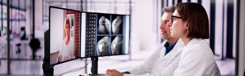 Two doctors are reviewing scans and consulting a patient via video call.