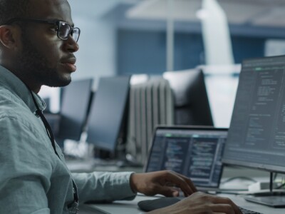 Male Software Engineer Developing App on a multi-monitor computer.