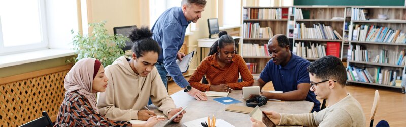 English language teacher helping immigrant students with lesson in library.