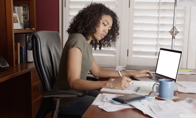 Woman works on paper documents and laptop while sitting in office