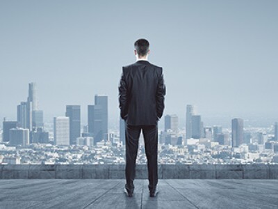 Man in a business suit stands with his back to the camera, staring at the city skyline