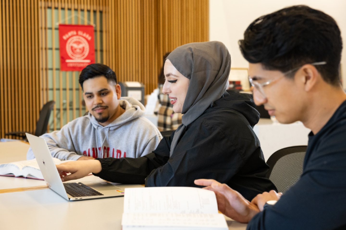 Two men and one woman seated at table studying with books and laptop