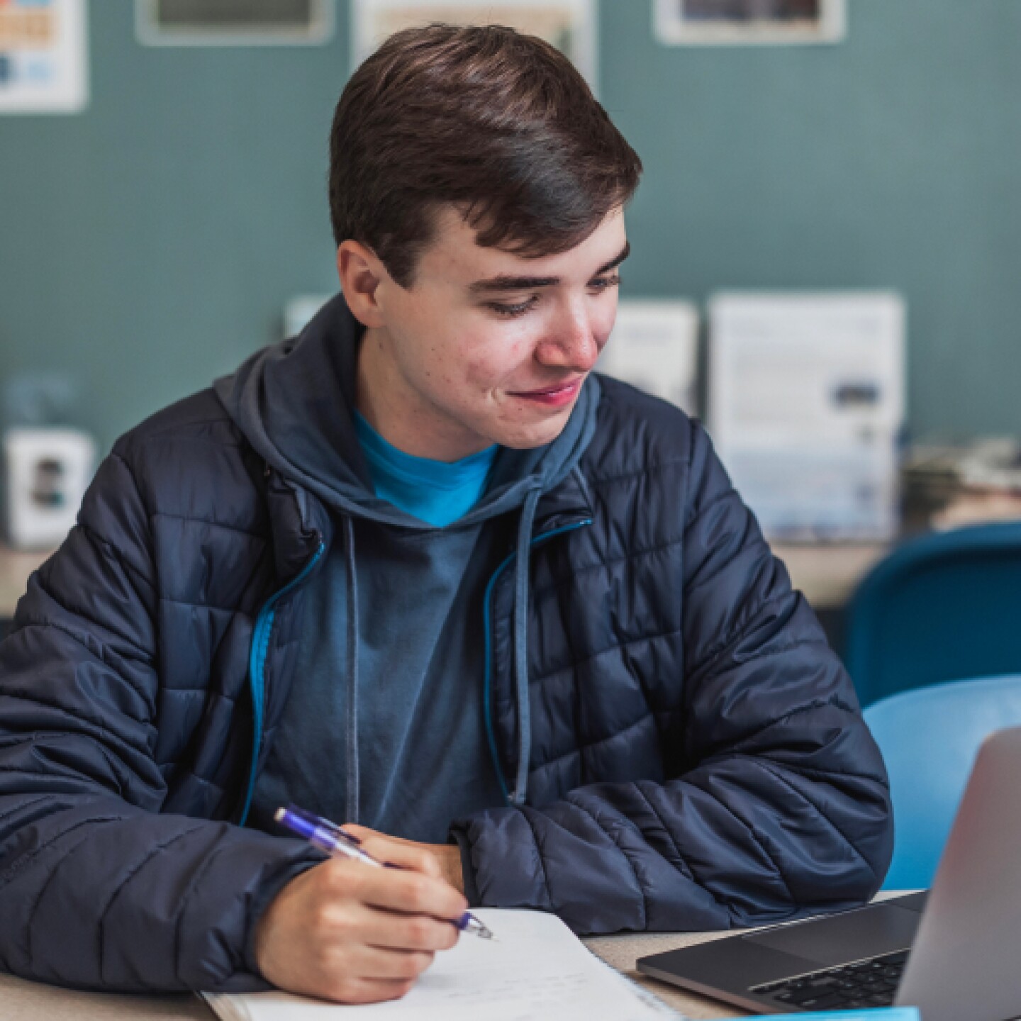 A male CSUMB student looking down at laptop screen while taking notes in notepad.
