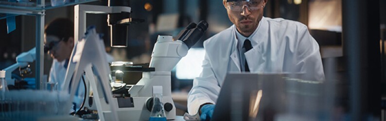 Scientists in a lab examine microscope samples and computer screens