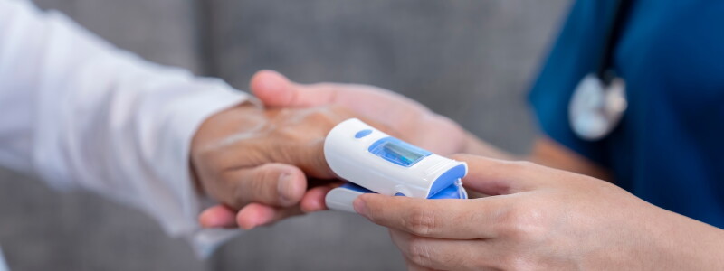 A nurse in uniform, with stethoscope, reads a patient's pulse oximeter