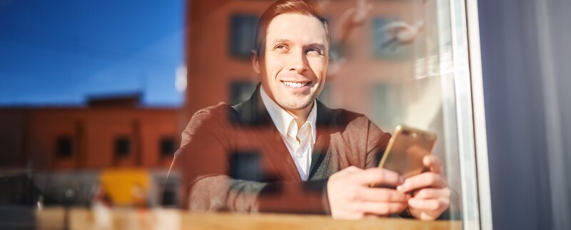 Male with phone in hand sitting in cafe, reflection of building in glass