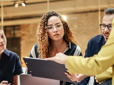 A diverse group of professionals engaged in a focused team meeting, reviewing a document together.