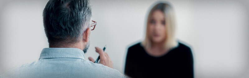 Close-up of a therapist holding a pen talking to his blurred female patient