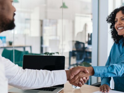 Man and woman shake hands across a desk after an interview.