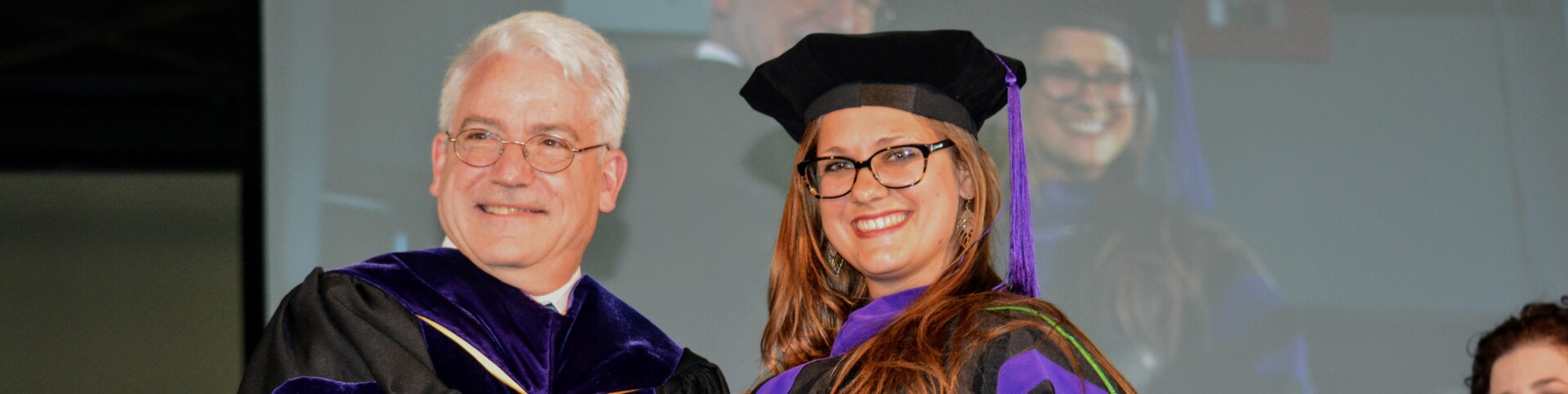 Graduation Ceremony woman in cap and gown shanking a mans hand