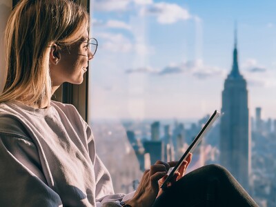 Woman with tablet looking out of a window at New York city