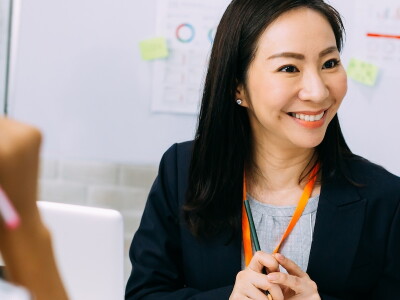 A smiling Asian woman collaborates with teammates in a meeting room.