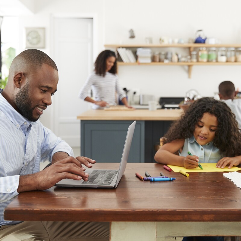 Parent sits at table with daughter on laptop
