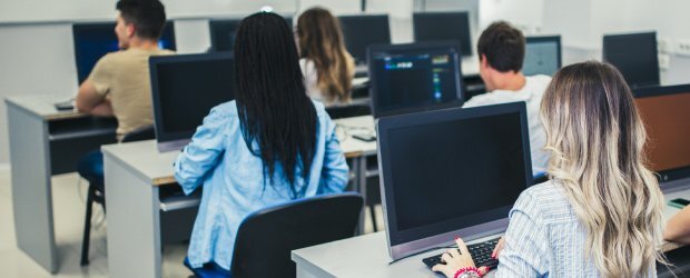 five-people-sitting-at-black-computers-facing-away-from-camera-in-three-rows