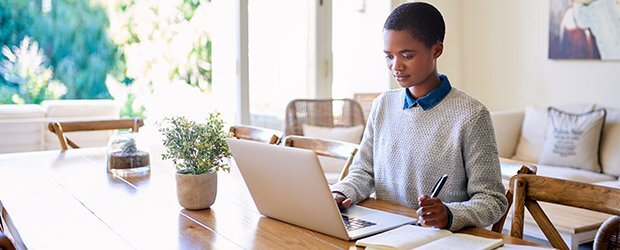 person-in-grey-sweater-blue-collar-sitting-at-wood-table-on-computer-taking-notes
