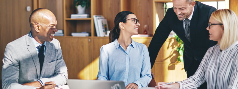 A team of accountants dressed in business attire are gathered at a table, smiling at each other.
