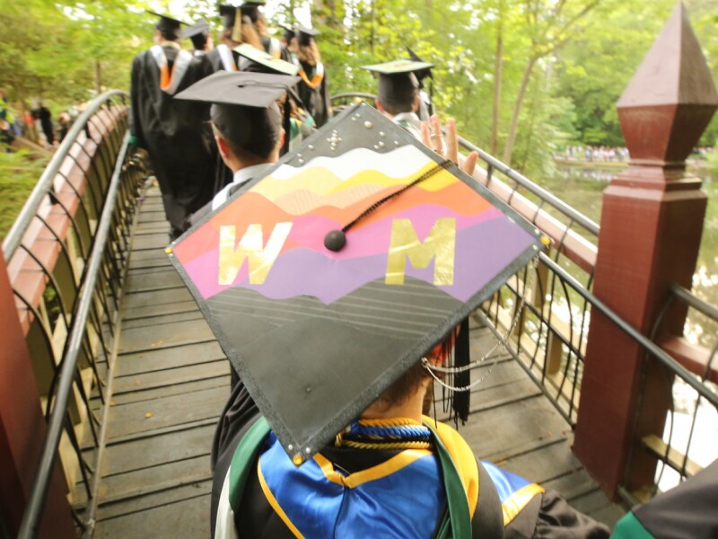 Graduates in cap and gown crossing the Crim Dell Bridge