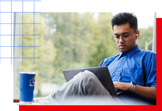 A male KU student reviews tuition information on a laptop with a Jayhawk cup sitting in front of him.