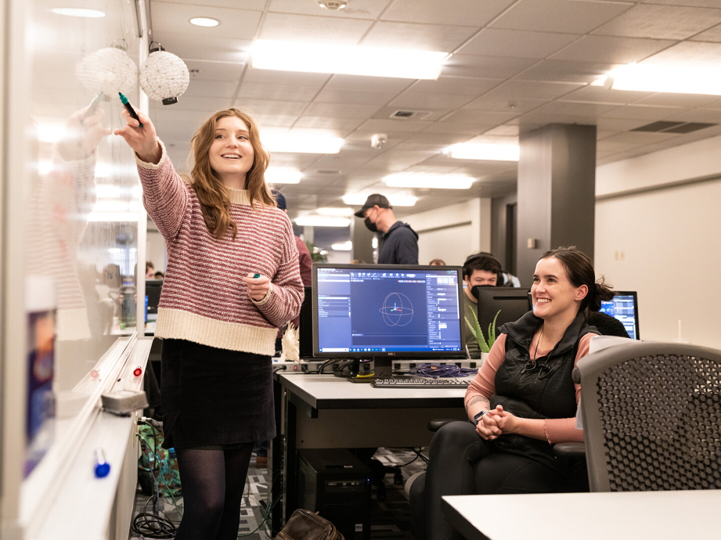 Woman presenting ideas on a whiteboard to colleagues in a collaborative workspace.