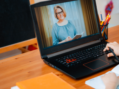 Kid in blue shirt sitting at computer watching teacher