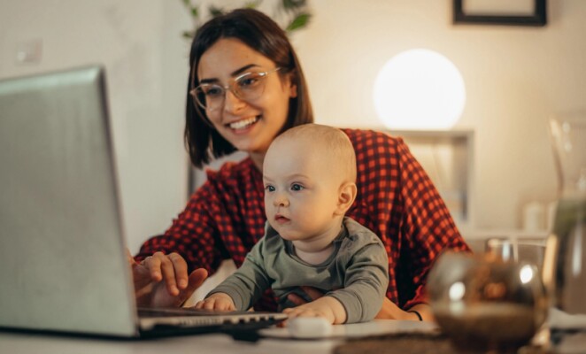 Woman holding baby and working on laptop