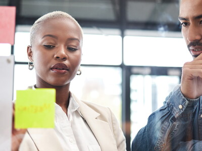 Man and woman looking at ideas on sticky notes at workplace.
