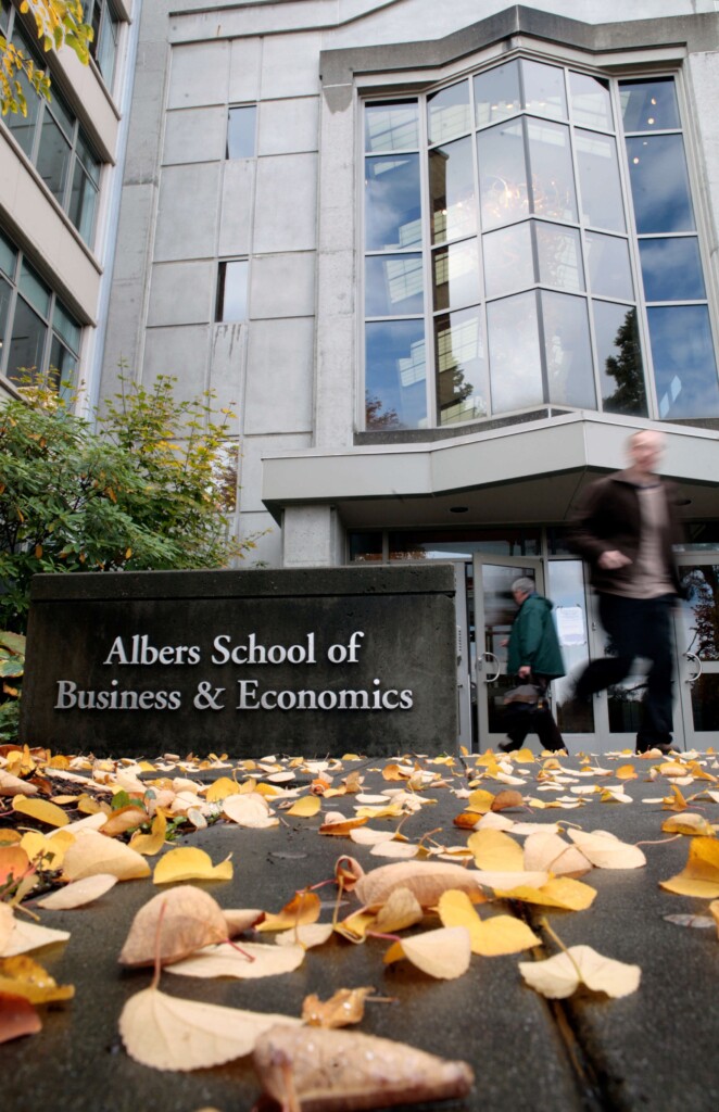 Front facade of the the Albers School of Business & Economics with students walking in front and leaves on the ground