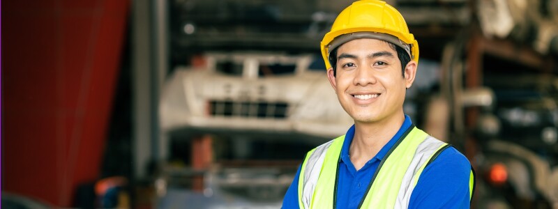An engineer wearing a hard-hat smiles in a factory work setting