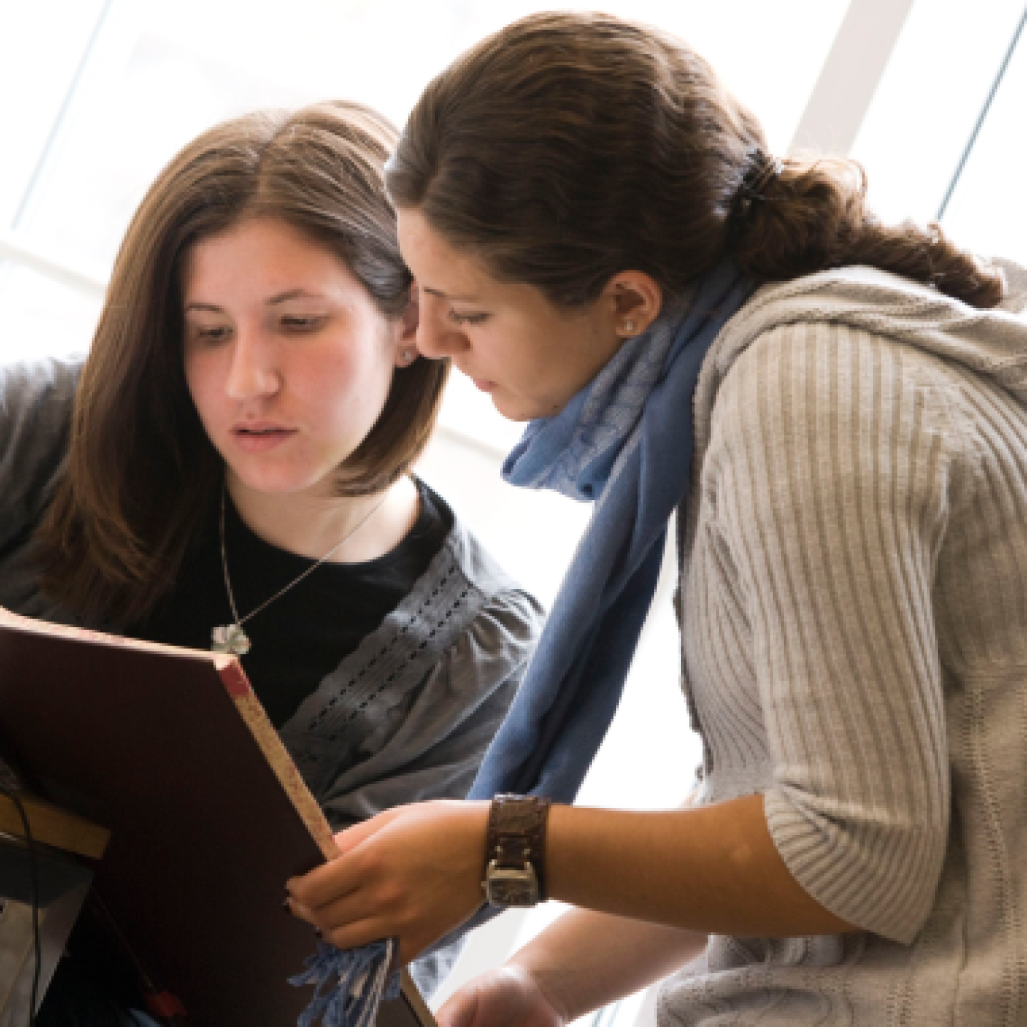 Two female Yeshiva University students huddle together, reviewing a textbook.